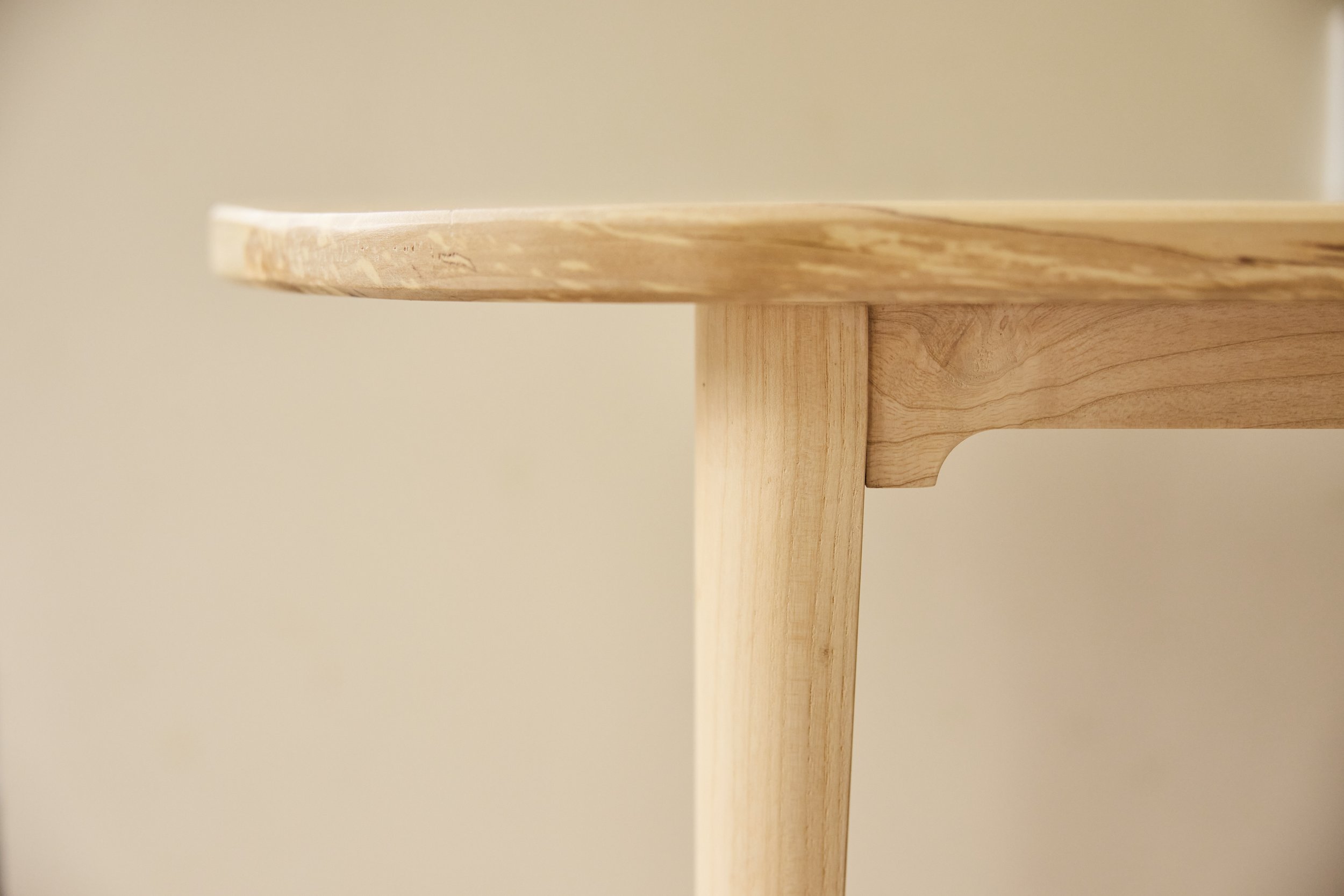 Close-up of the edge of a solid wooden handmade bench against a plain background.