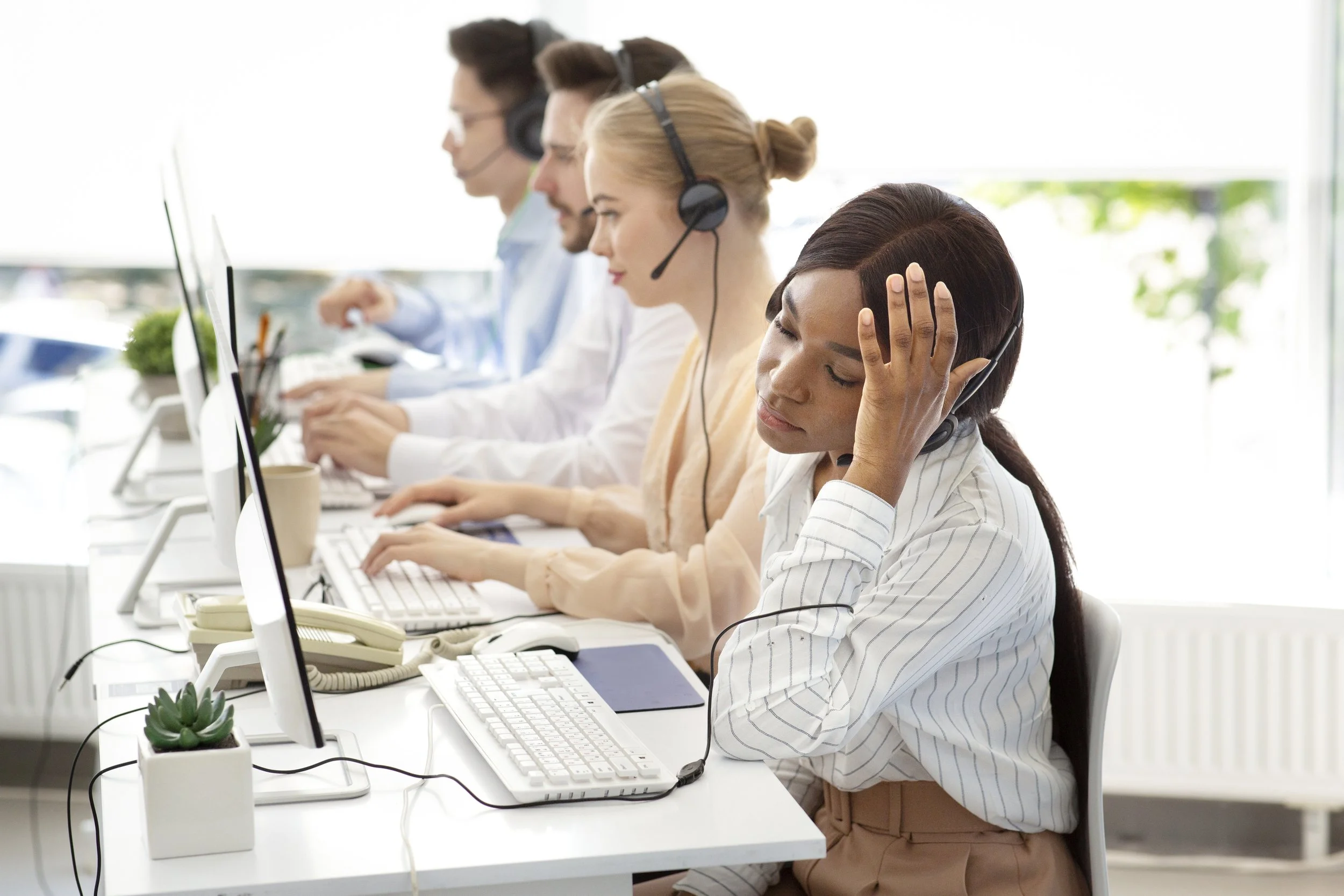 Several customer service representatives working at their desks with headsets, phones, and computers in an office.