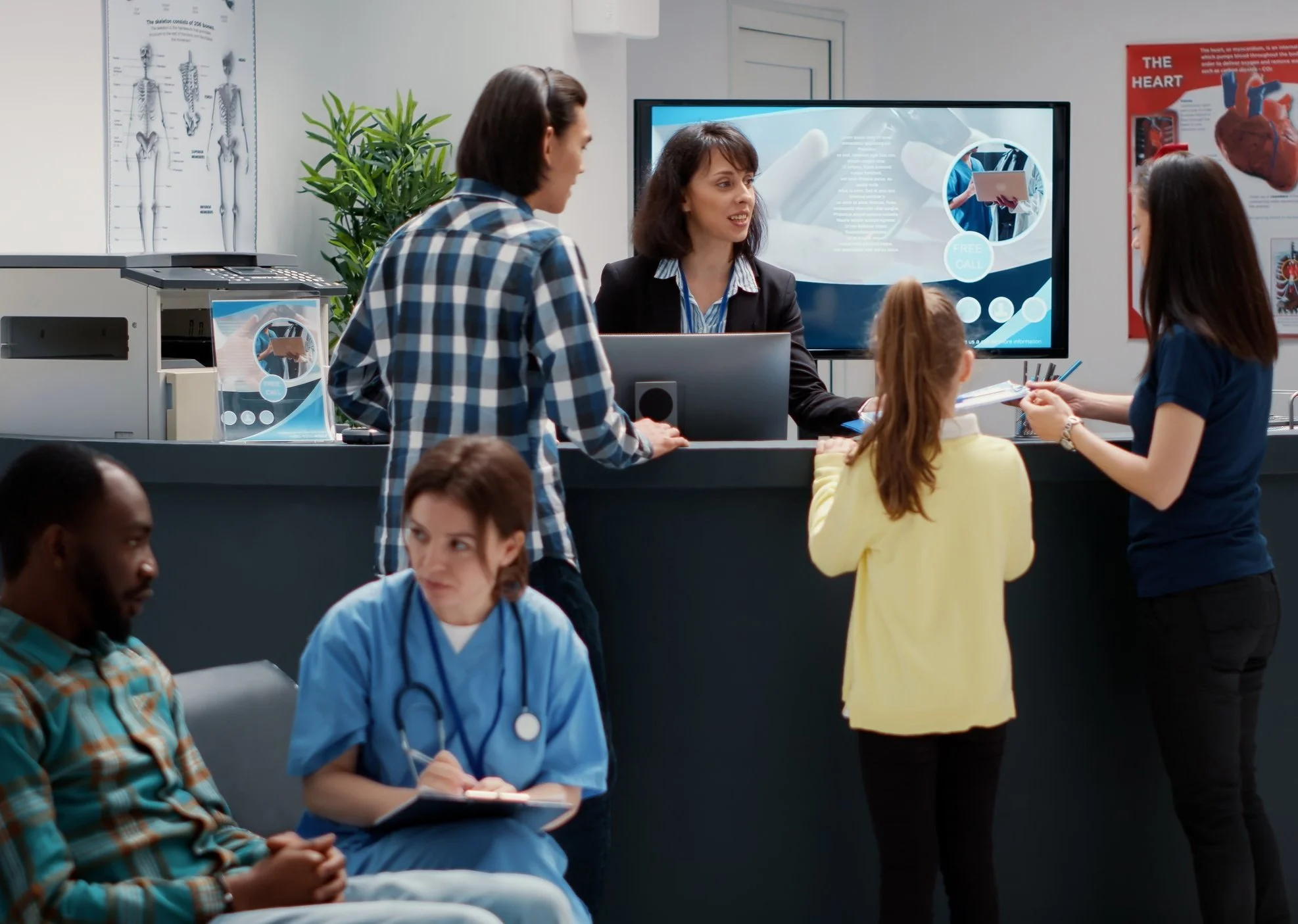 People in a medical waiting room with a receptionist, including a nurse taking notes, and a child with an adult at the desk.