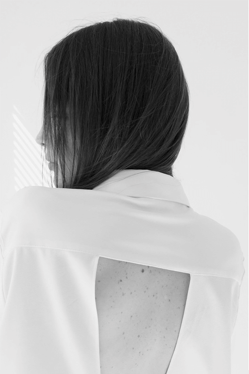 A woman with dark hair seen from behind, wearing a white top with a large cutout on the back.