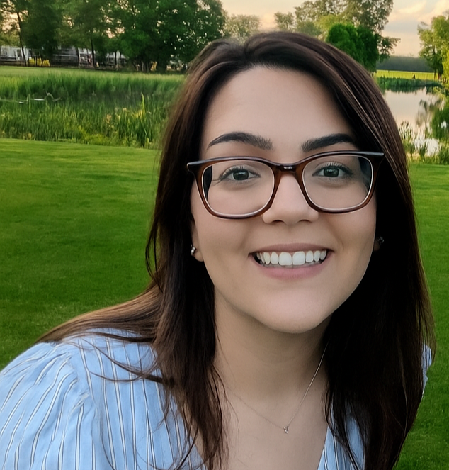 Women smiling outdoors near a lake and green grass.