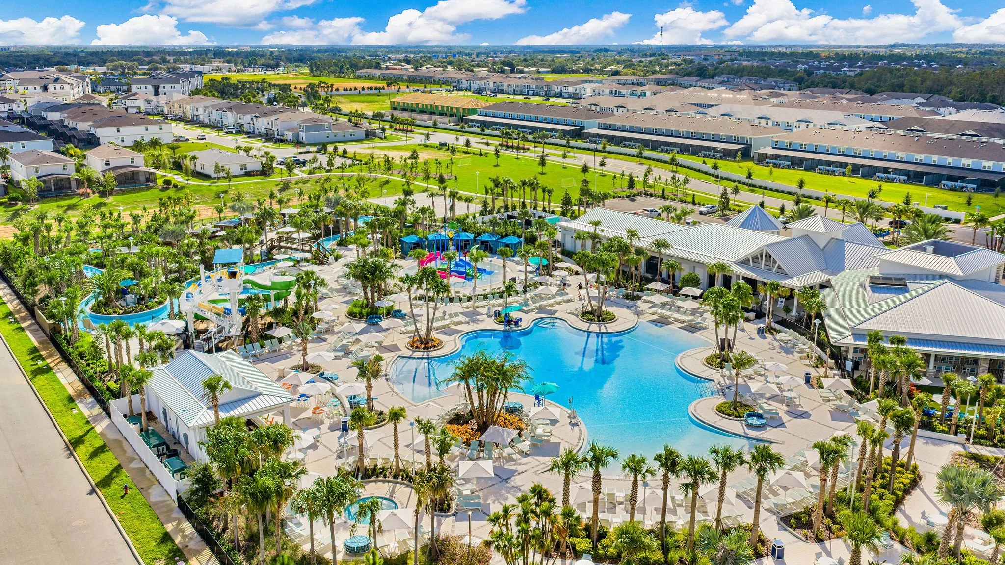 Aerial view of a Windsor Cay Resort swimming pool area with water slides, surrounded by palm trees, lounge chairs, and nearby houses.
