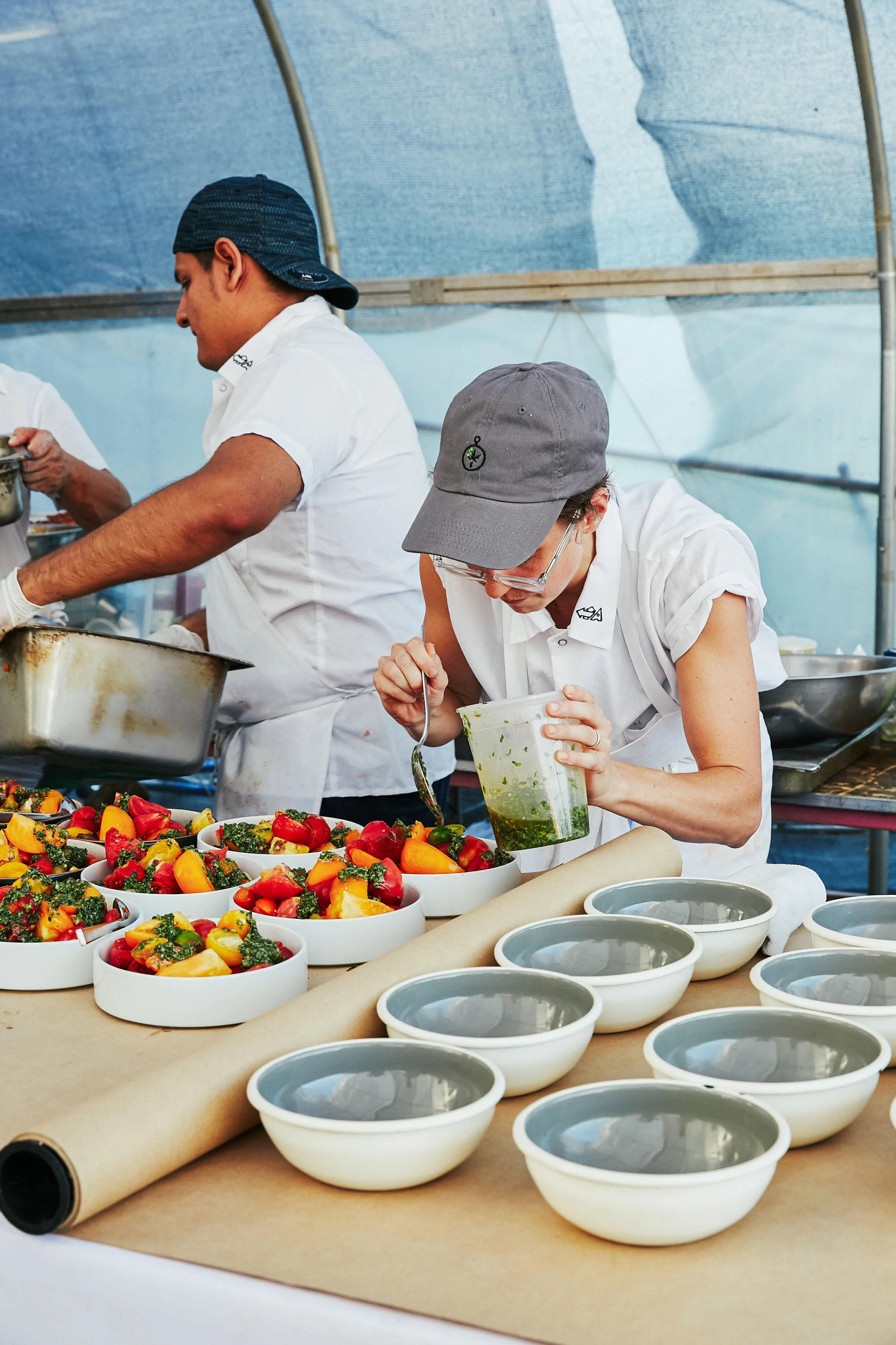 Two chefs preparing colorful fruit salads in a kitchen or food stall, with bowls of watermelon, pineapple, and other fruits on a table.