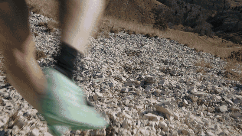 Close-up of a person running on rocky terrain, showing green running shoes and black socks.
