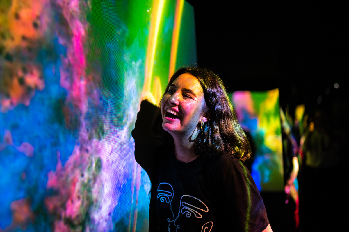 Woman smiling and looking at colorful digital art display at an art exhibit or gallery.