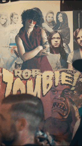 A woman with curly black hair and sunglasses sitting behind a poster for the movie 'The Rocky Horror Picture Show,' with other posters of the film in the background.