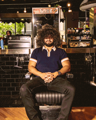 Man with curly hair and beard sitting on a barber chair inside a barbershop