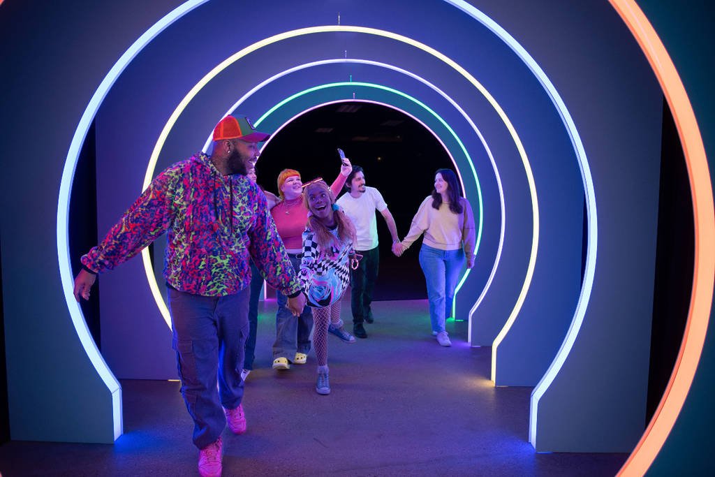People walking through a colorful, neon-lit tunnel and taking selfies.
