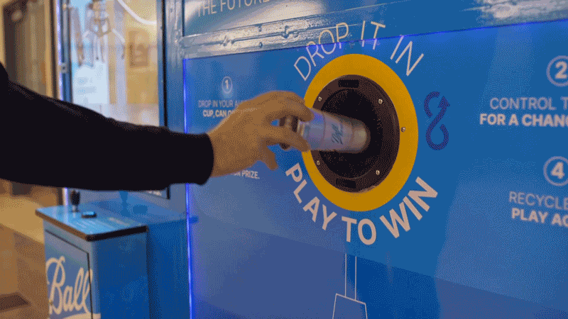 Person inserting a can into a recycling machine with instructions to drop it in and play to win.