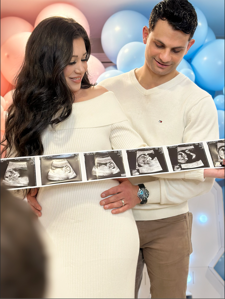 Happy pregnant woman and her partner looking at ultrasound images in a room decorated with balloons.