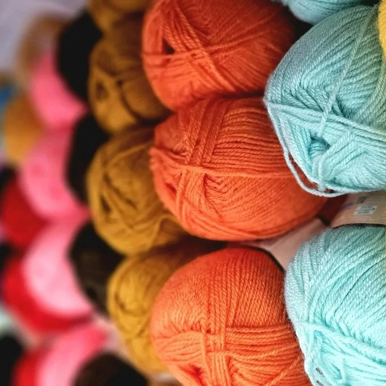 Colorful balls of yarn arranged in a display, including orange, light blue, yellow, black, pink, and red.