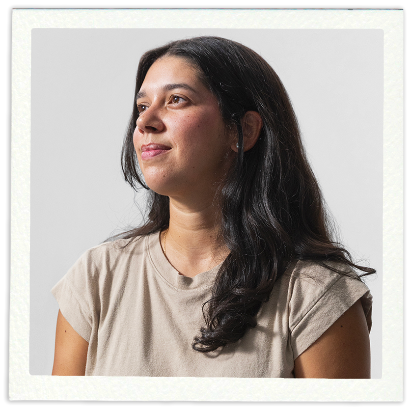Portrait of a woman with long, dark hair, wearing a beige T-shirt, looking slightly to the left, against a plain light background.