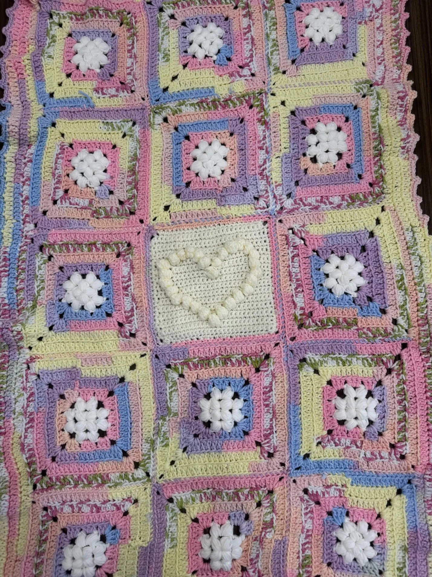 Colorful crocheted blanket composed of multicolored granny squares with white flower centers and a heart design in the center square.
