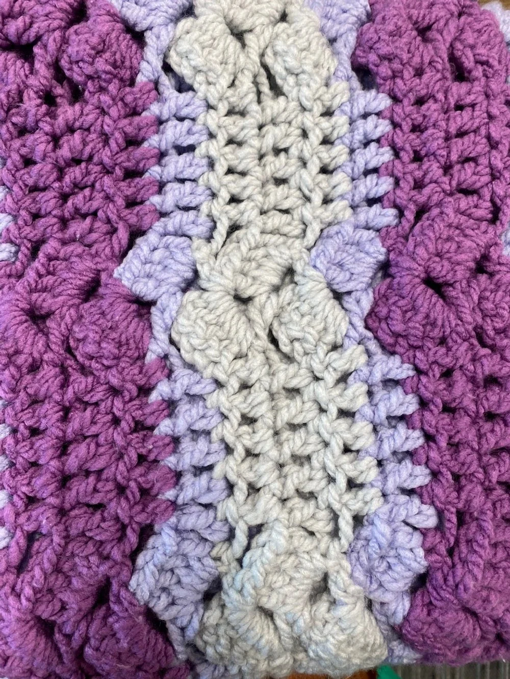 Close-up of a purple, lavender, and white crocheted blanket with textured patterns.