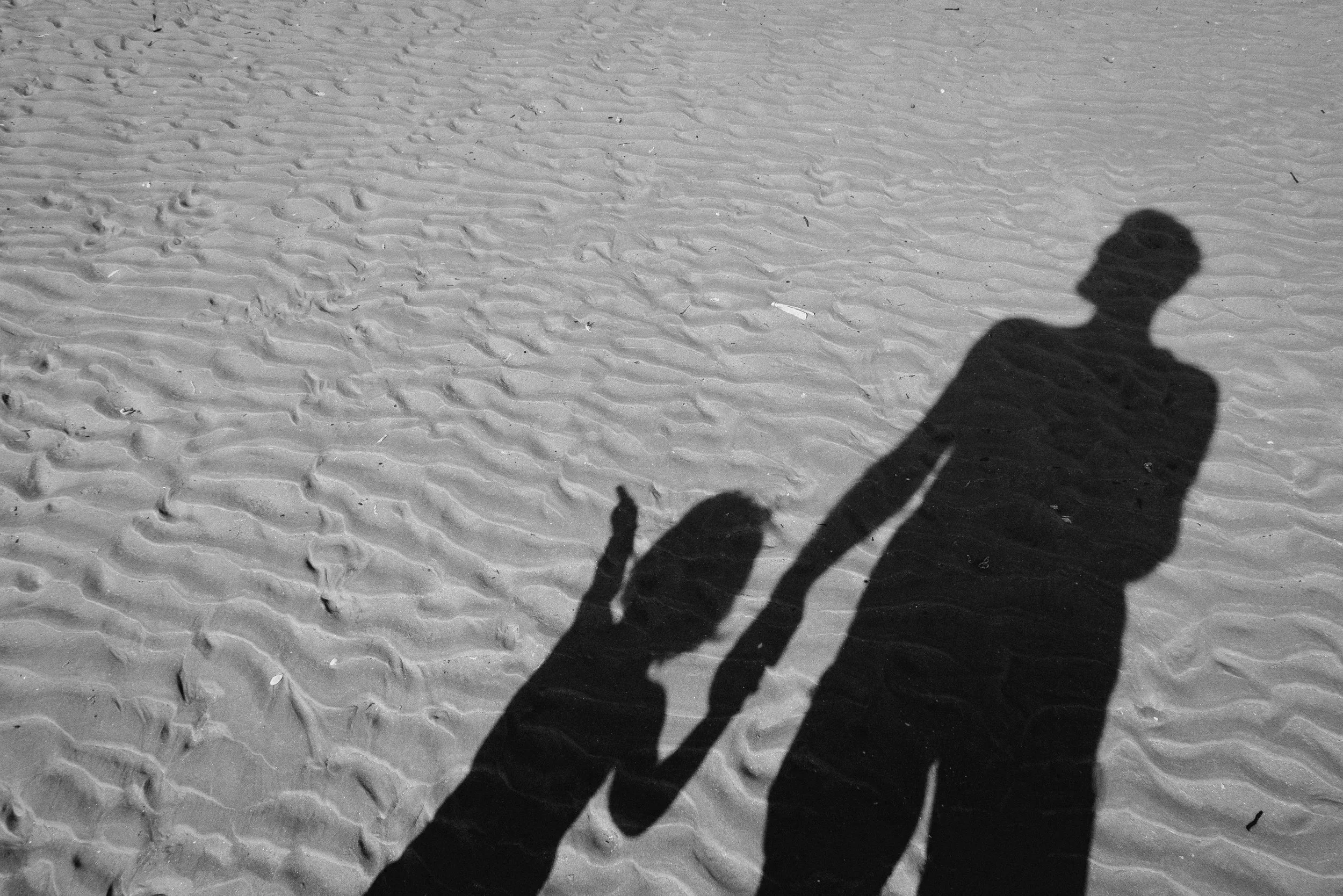 Shadow of an adult and a child holding hands on a sandy beach