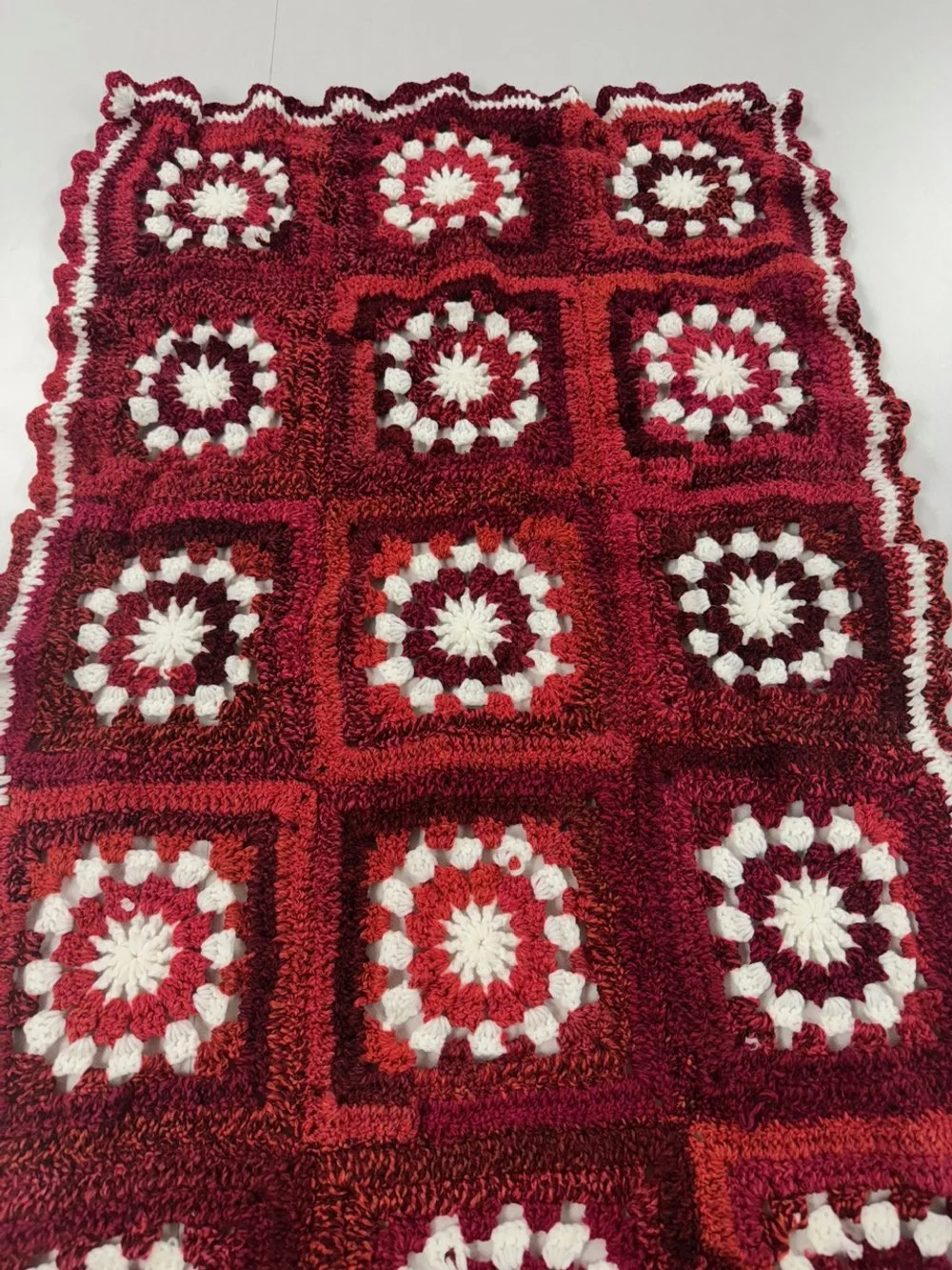 Close-up of a handmade crocheted blanket with red, white, and black granny square patterns.