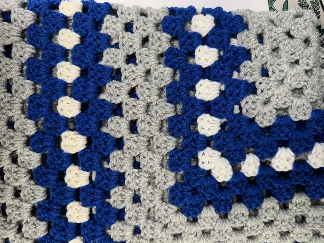 Close-up of a crocheted blanket made with gray, white, and blue yarn in a floral pattern.
