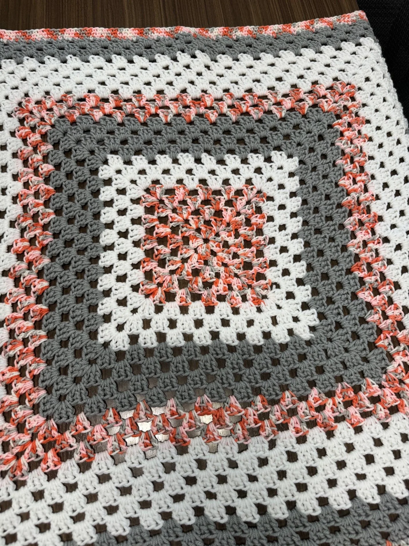 Close-up of a multicolored crochet blanket with white, gray, and pink yarn, featuring a square pattern.