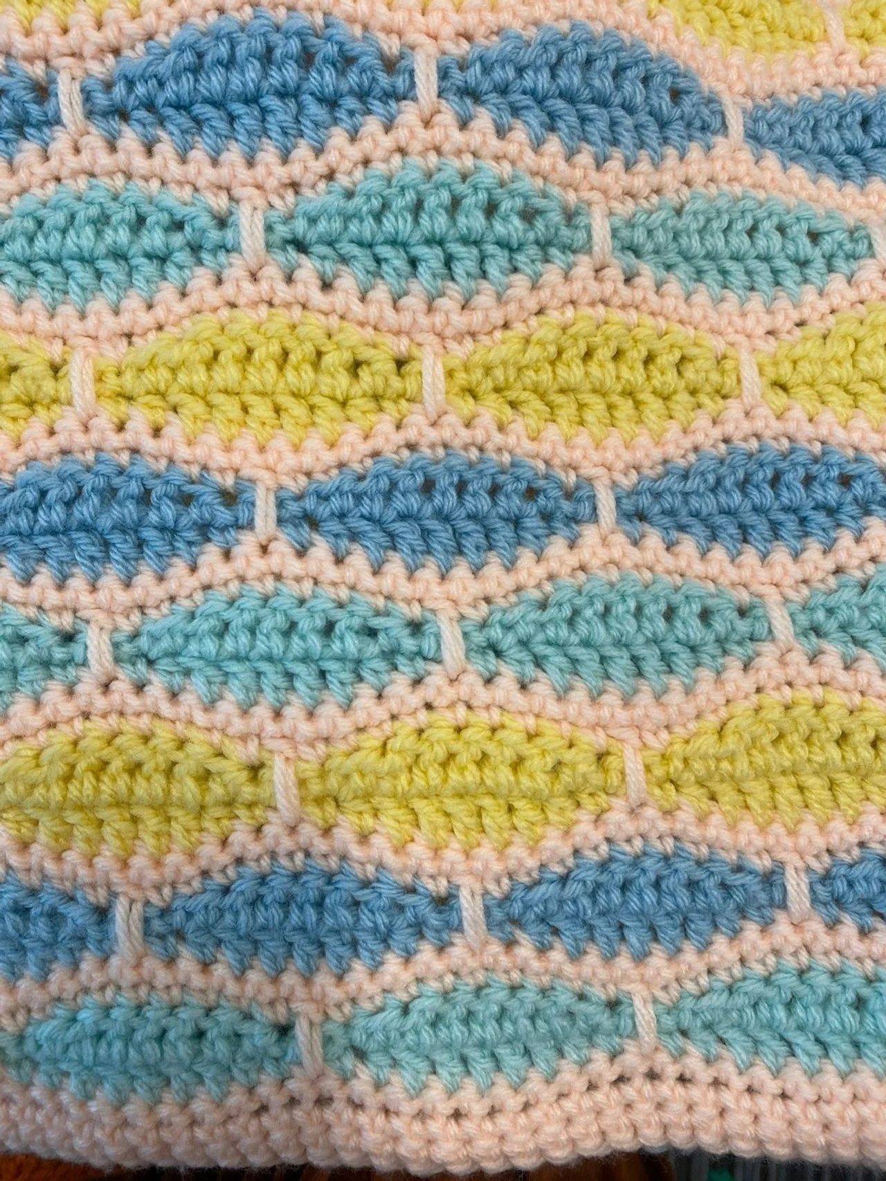 Close-up of a colorful crocheted fabric with a pattern of rainbow-colored semi-circles in blue, yellow, pink, and green.