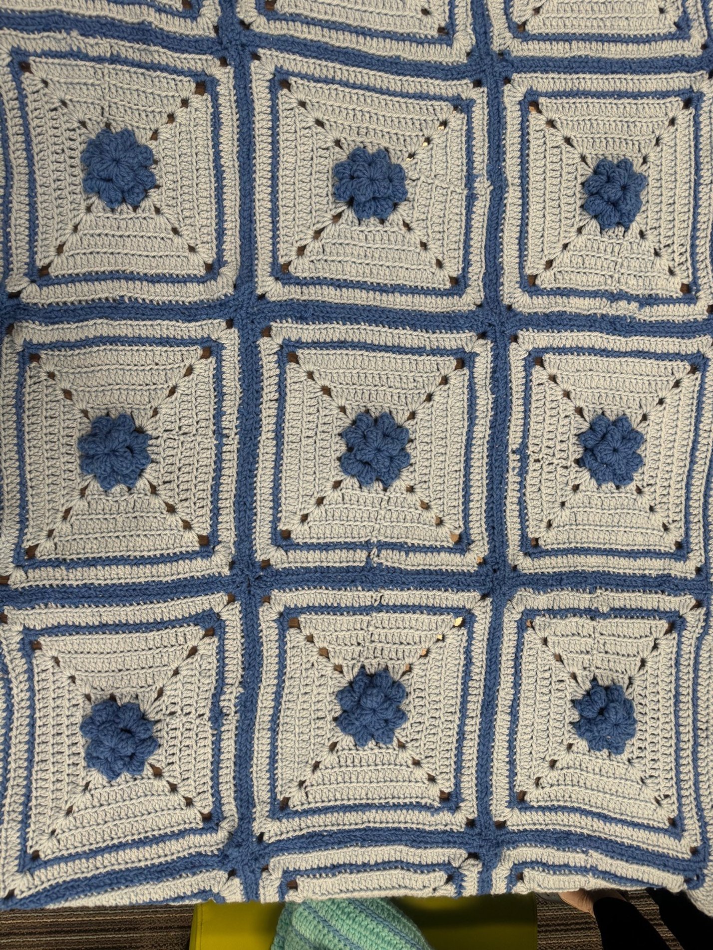 A crocheted blanket made of square patches, each with a blue flower in the center, surrounded by beige and blue yarn.