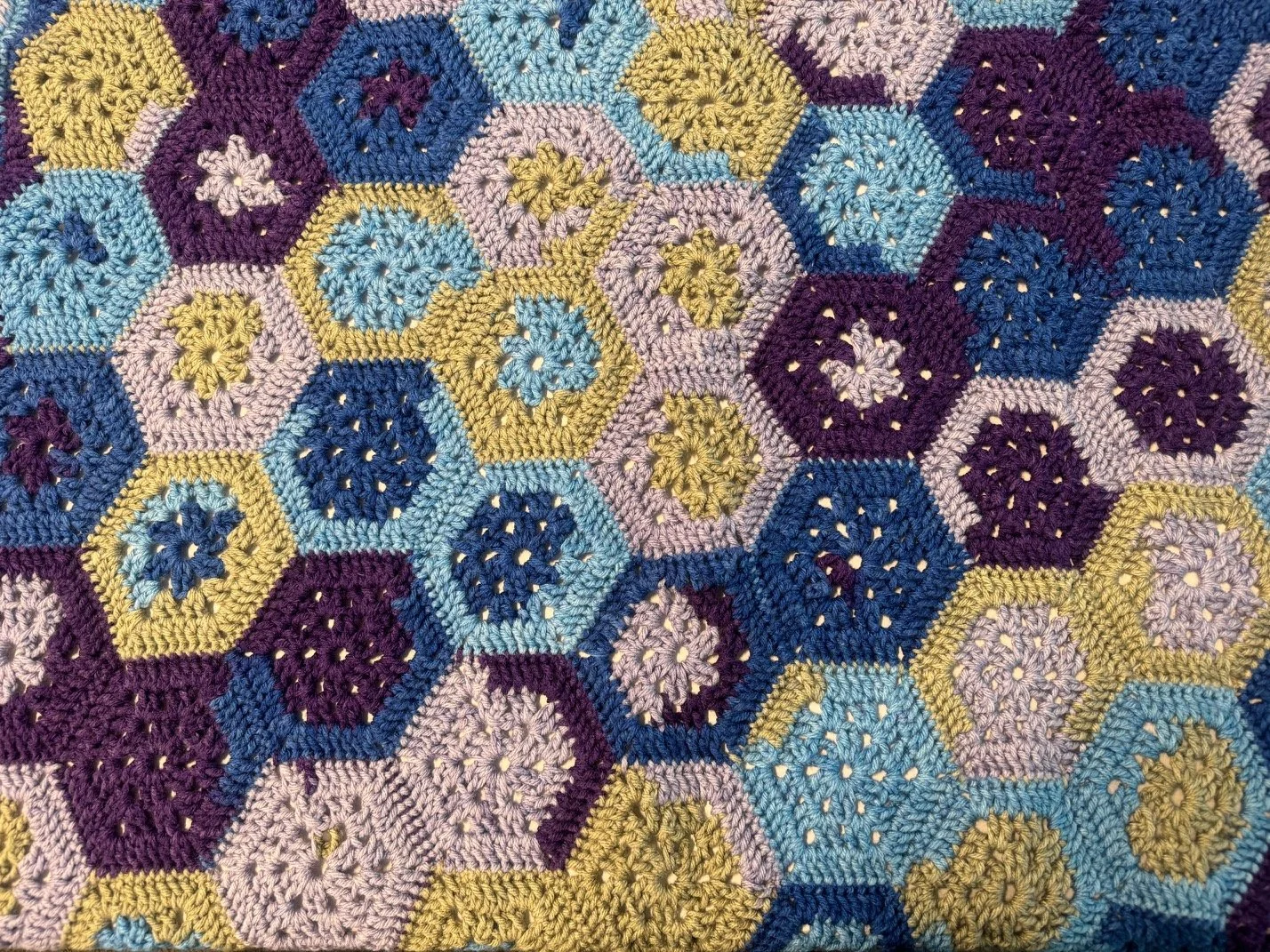 Close-up of a multicolored crochet blanket made of hexagon-shaped motifs in shades of blue, purple, pink, and yellow.
