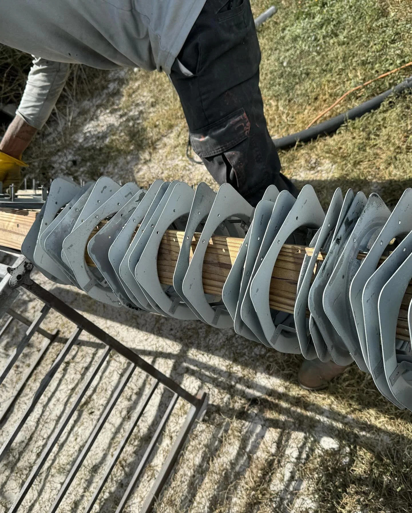 Close-up of metal brackets attached to a wooden beam, with a person working outdoors nearby.