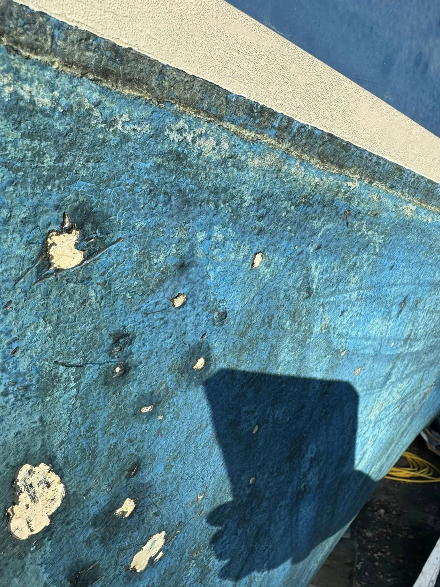 Close-up of a weathered blue surface with chipped paint and peeling spots, casting a shadow.