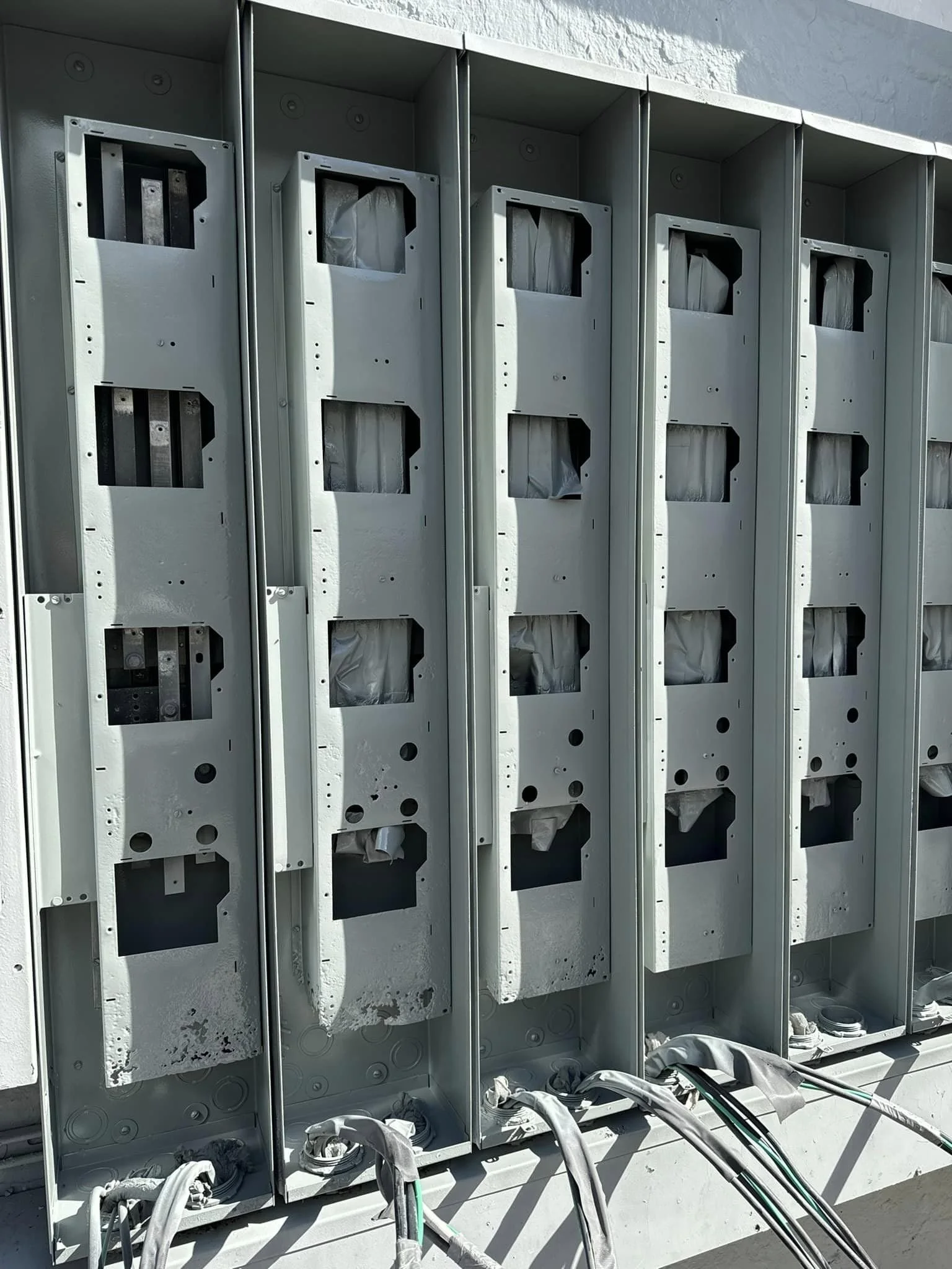 Empty outdoor electrical or telecom utility cabinets with some electrical wiring at the bottom, mounted on a concrete wall.