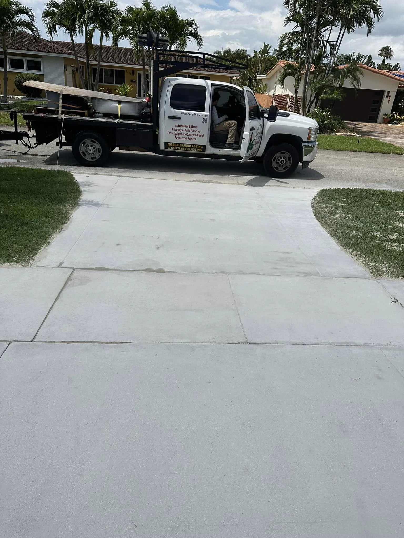 A white pickup truck parked on a suburban street, with a service sign on the door, surrounded by palm trees and houses.
