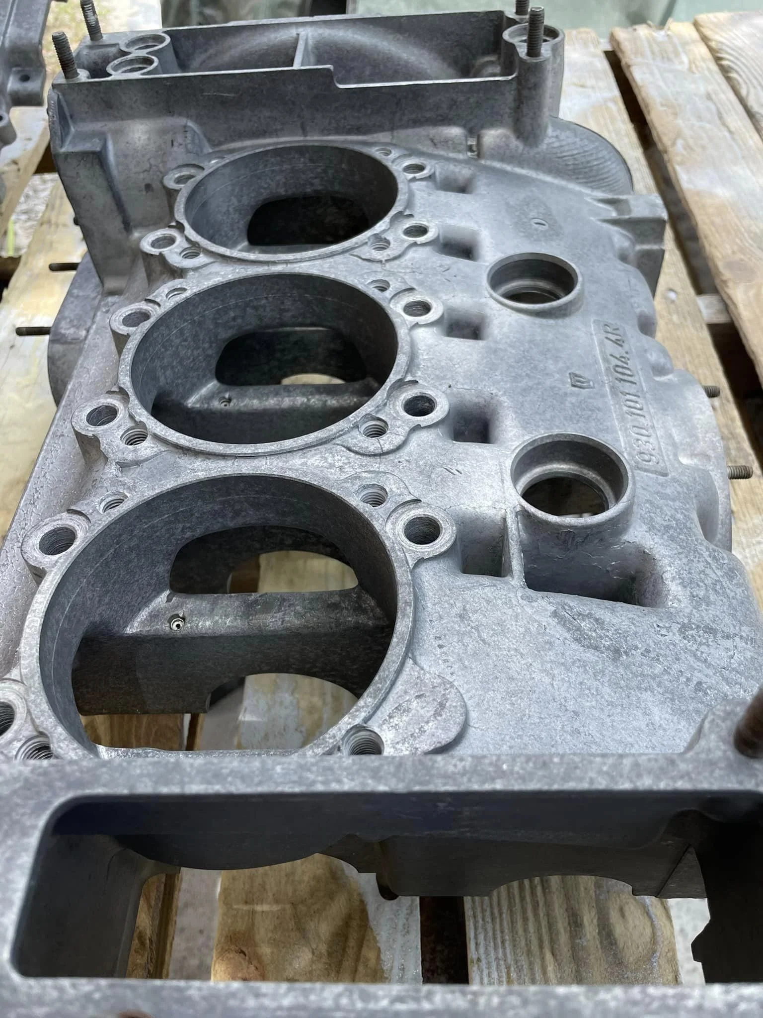 A metal engine cylinder head with four open cylinders, sitting on a wooden surface.