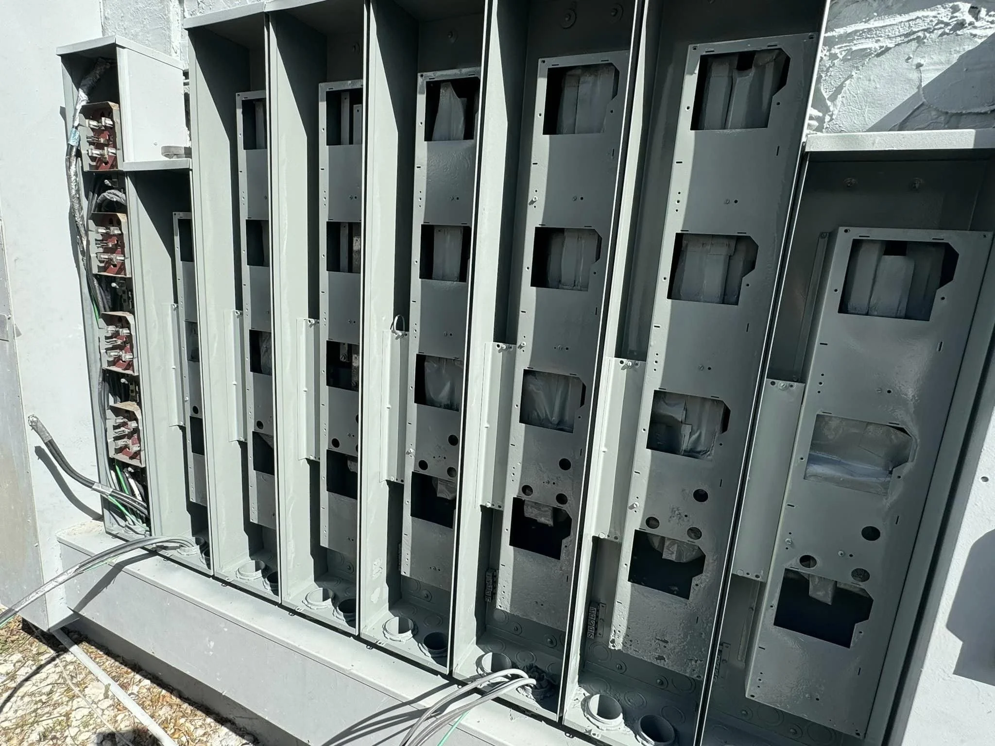 Empty electrical meter boxes on an outdoor panel with wiring visible on the left side under bright sunlight.
