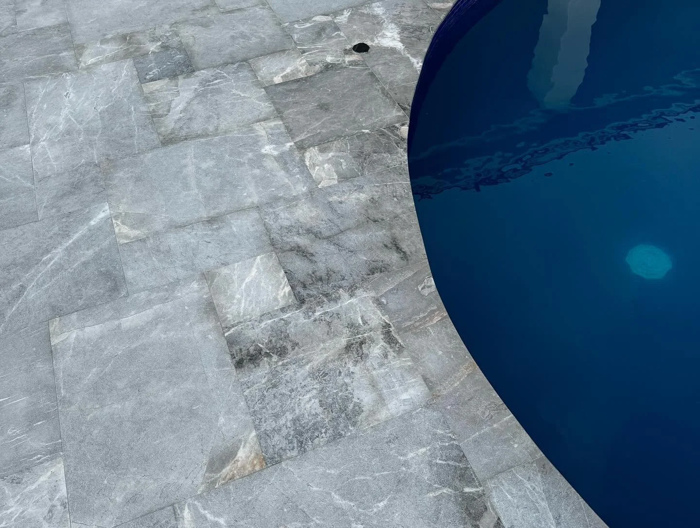 Part of a blue swimming pool on a gray stone tiled deck.