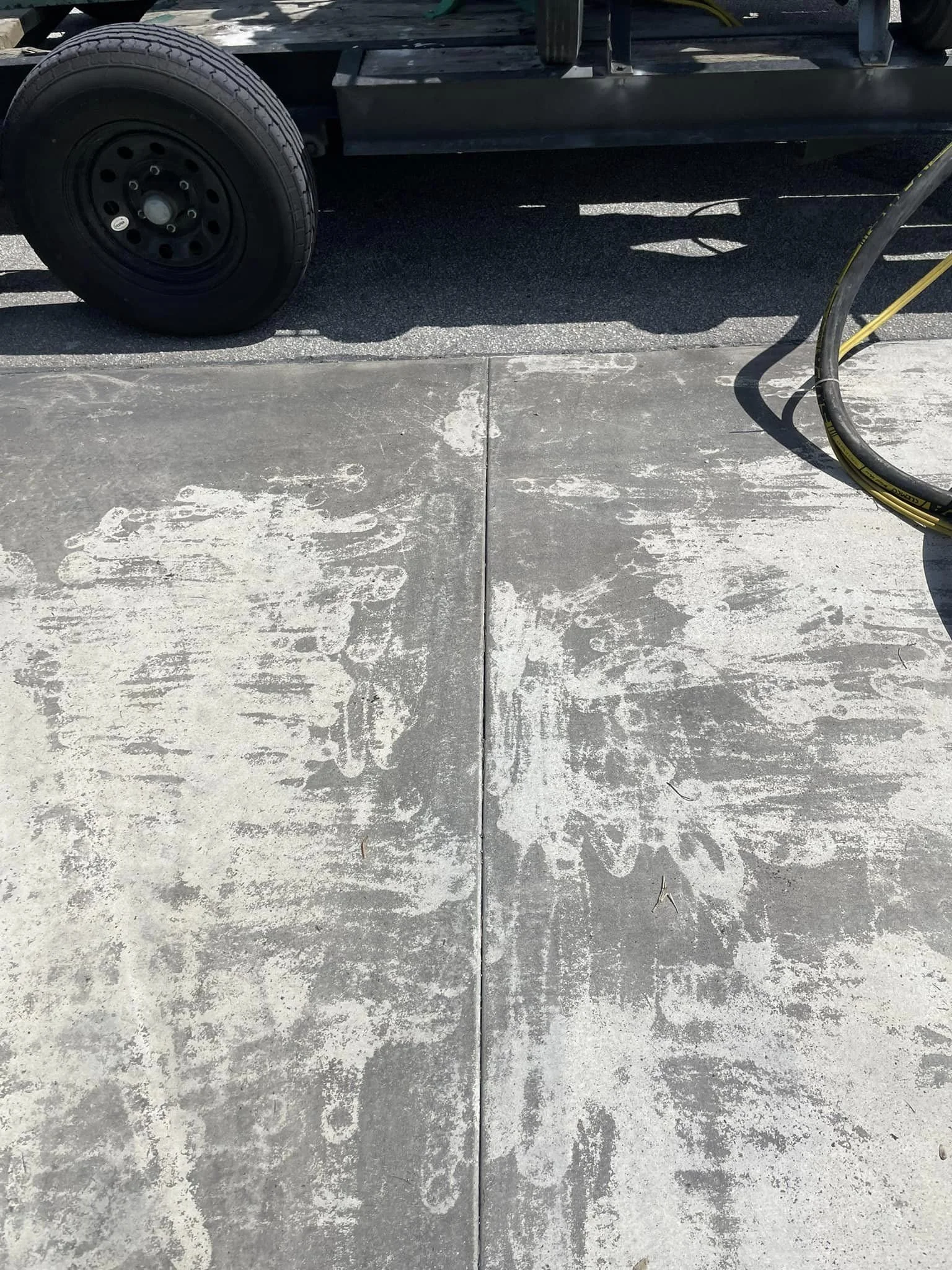 Concrete sidewalk with cleaning streaks and a vehicle with a tire on it, along with part of a hose or cable on the right side.