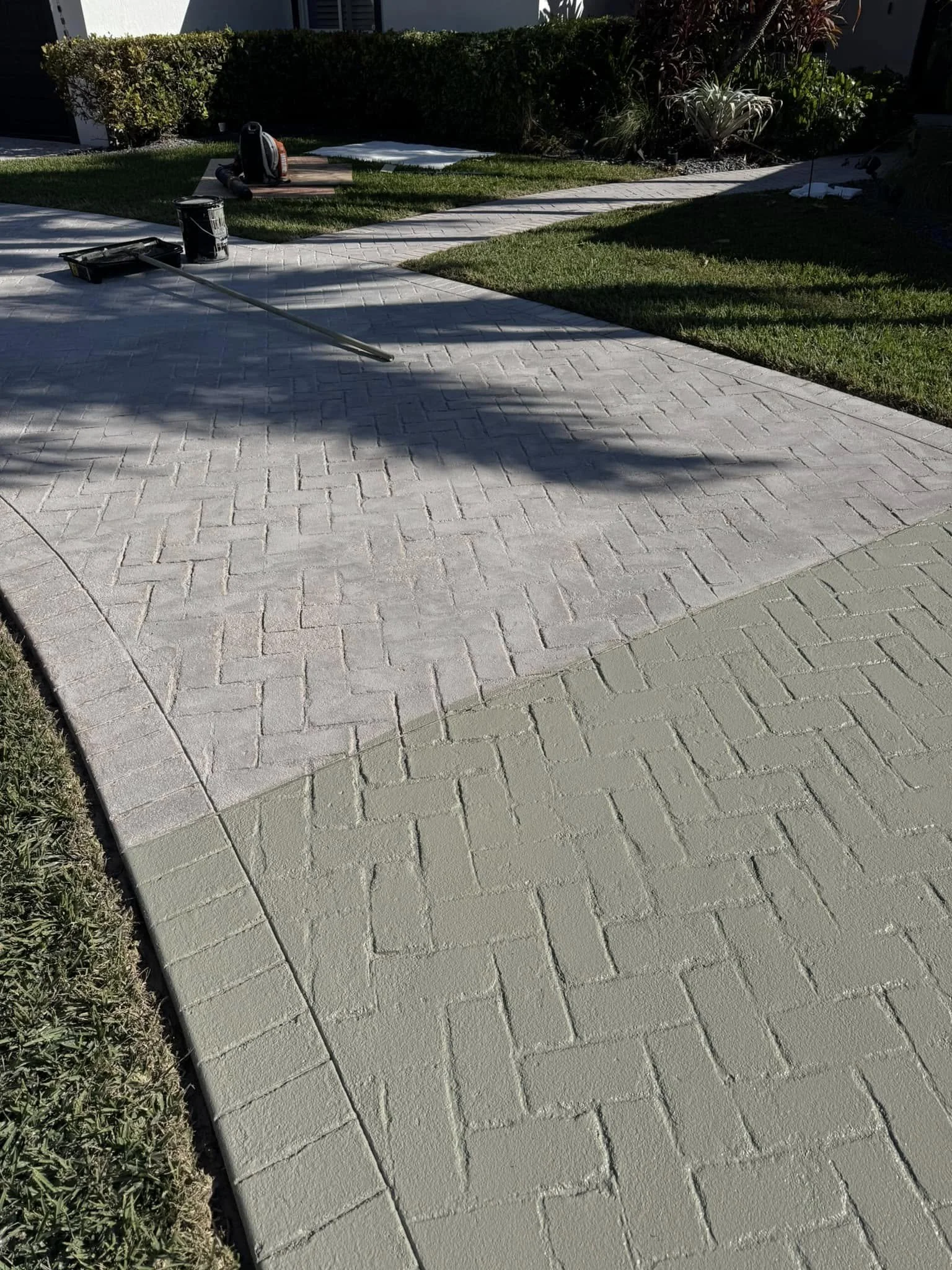 A newly paved outdoor walkway with different colored sections, surrounded by grass and landscaping with bushes and plants.