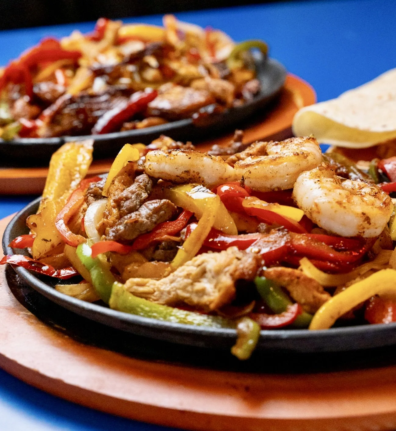 Close-up of sizzling fajitas with shrimp, beef, chicken, and colorful bell peppers on a cast iron skillet