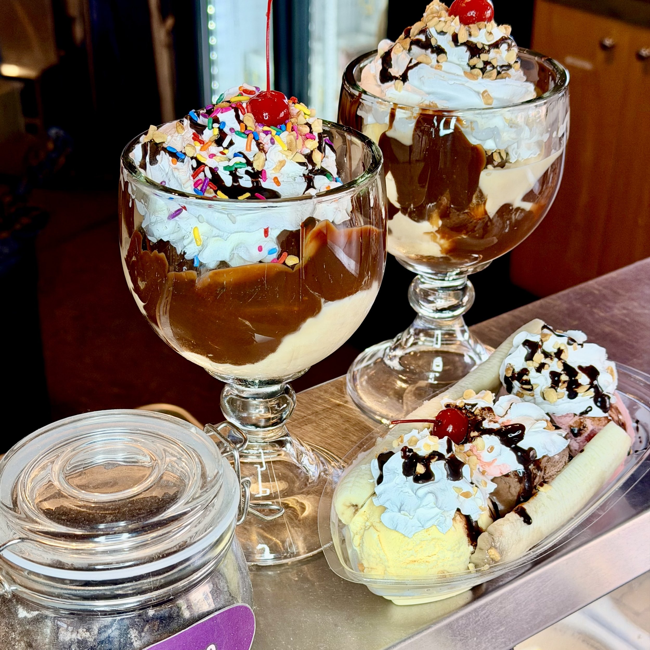 Two ice cream sundaes in goblets with layers of hot fudge, whipped cream, cherries and sprinkles.