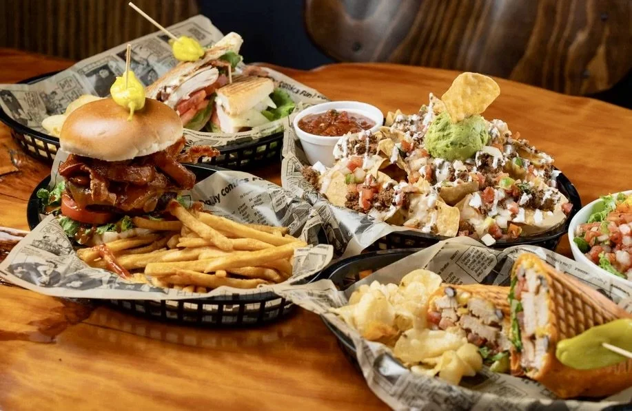 A table of food including a stacked hamburger and fries, nachos, salad and a quesadilla.