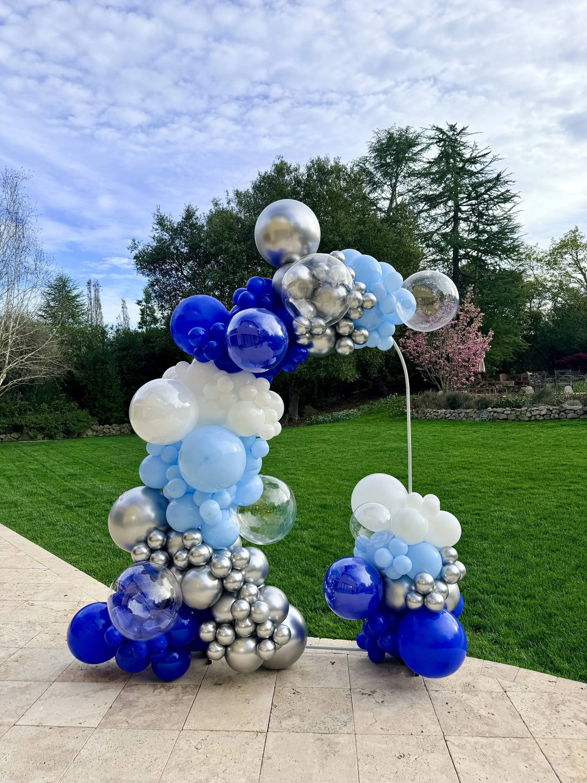 Sculptural blue, white and chrome silver balloon garland decorating a backyard graduation party in Atherton.