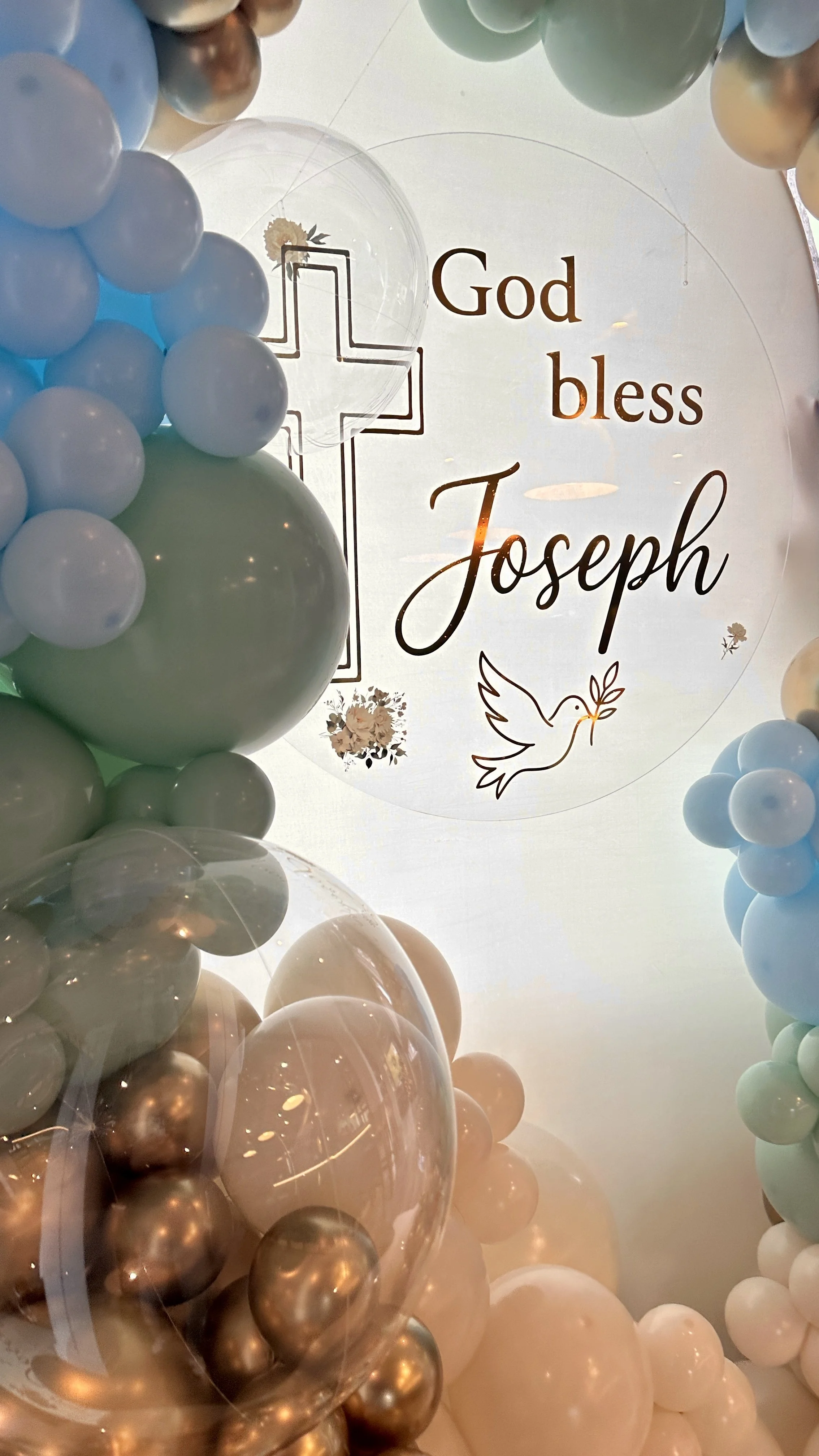 God bless lettering and a cross framed by blue, mint and metallic gold balloon clusters at a Sonoma baptism.