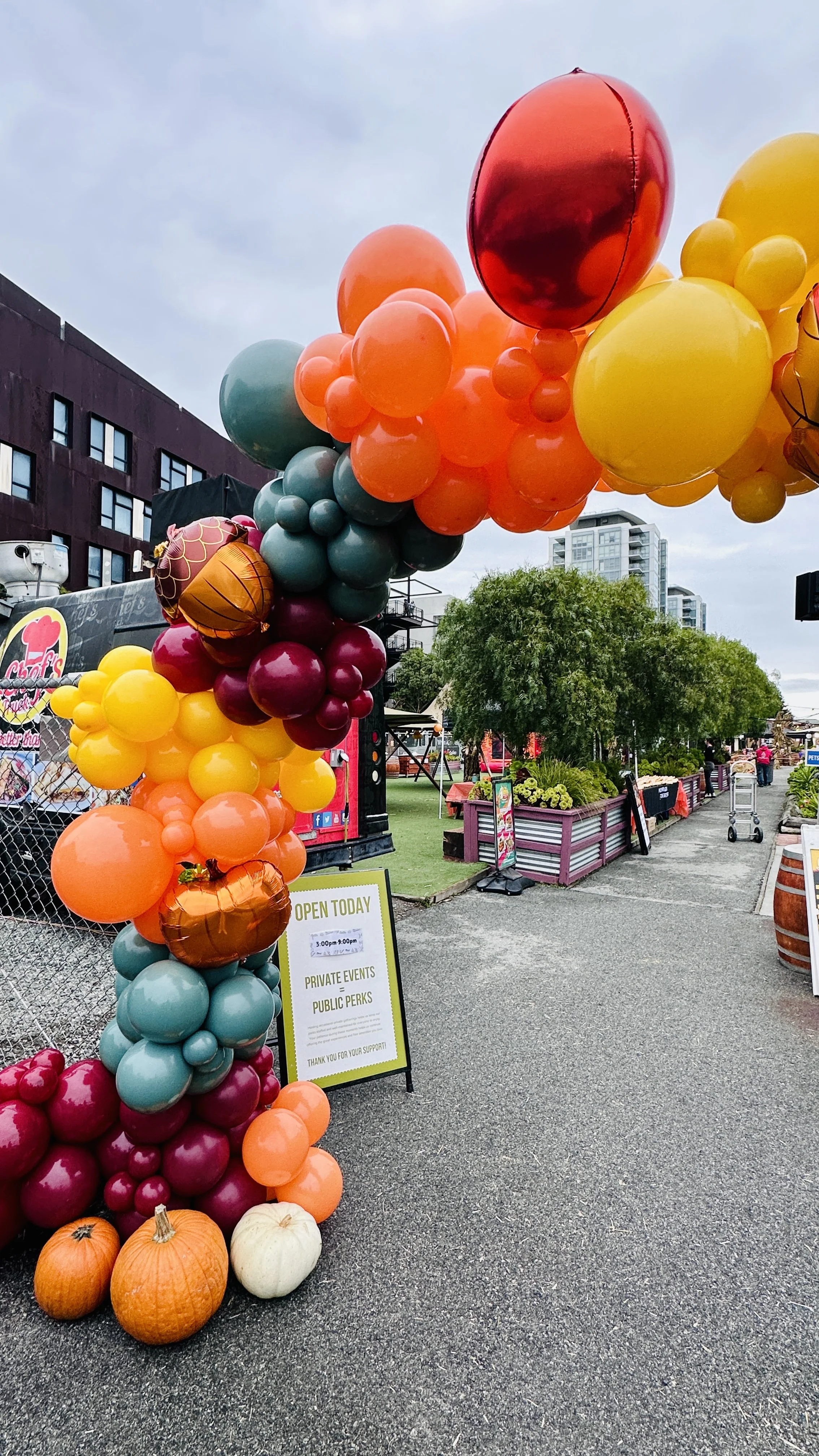 Burgundy, orange, yellow and teal balloon arch decorating an autumn event entrance in San Francisco.