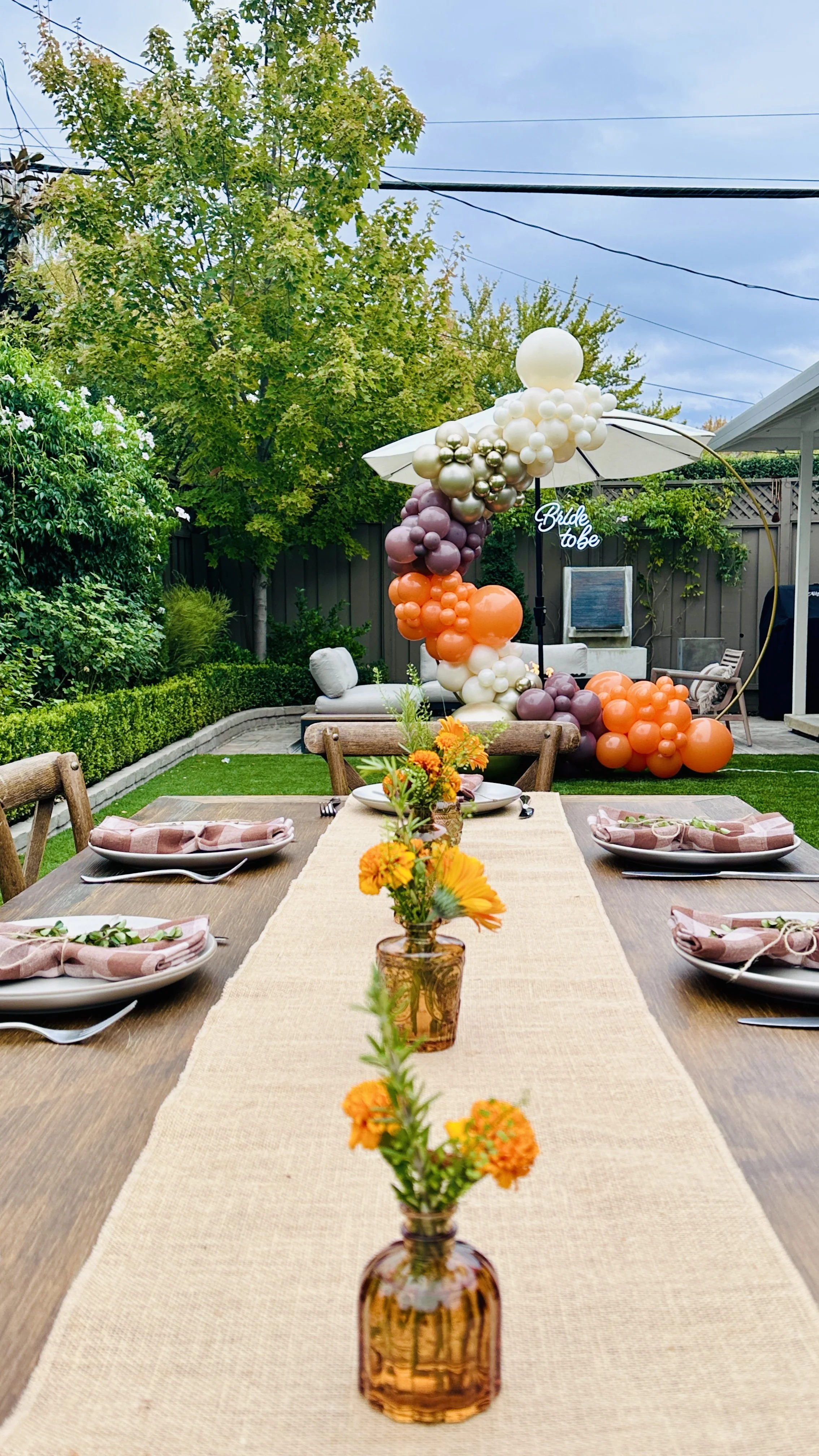 Outdoor bridal shower tables with orange flowers beneath an ivory and mauve balloon arch in Santa Clara.