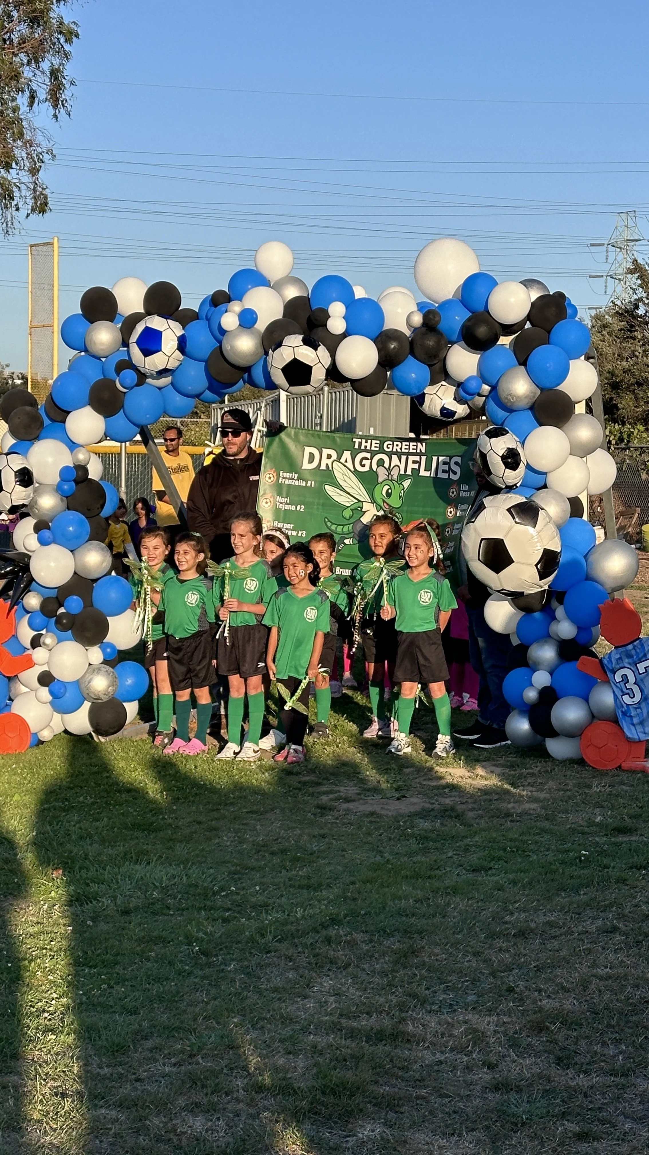 Blue, white and black soccer balloon arch framing a youth team photo at a San Bruno tournament.