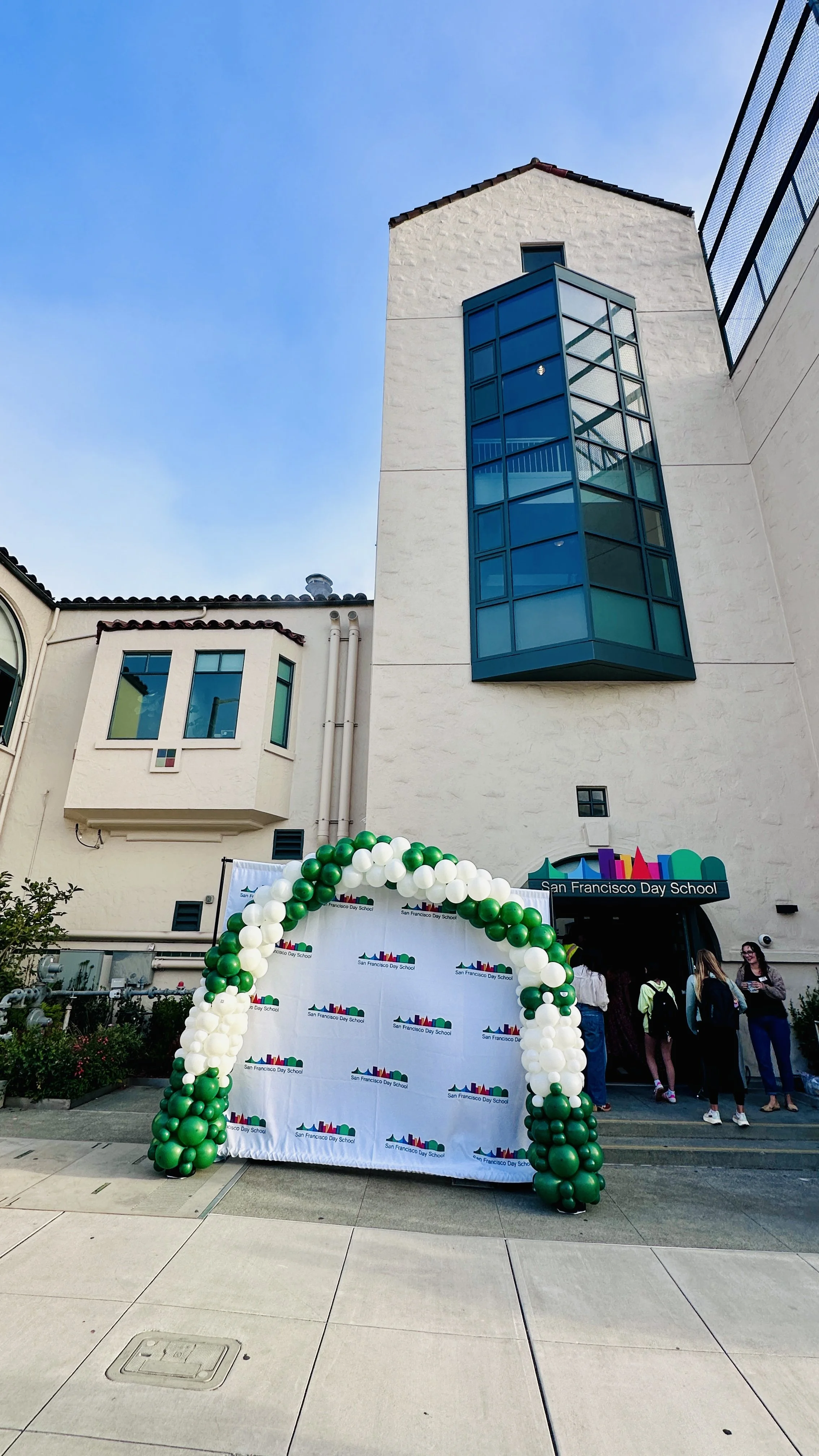 Green and white balloon entrance arch and school logo backdrop for the first day of school in San Francisco.