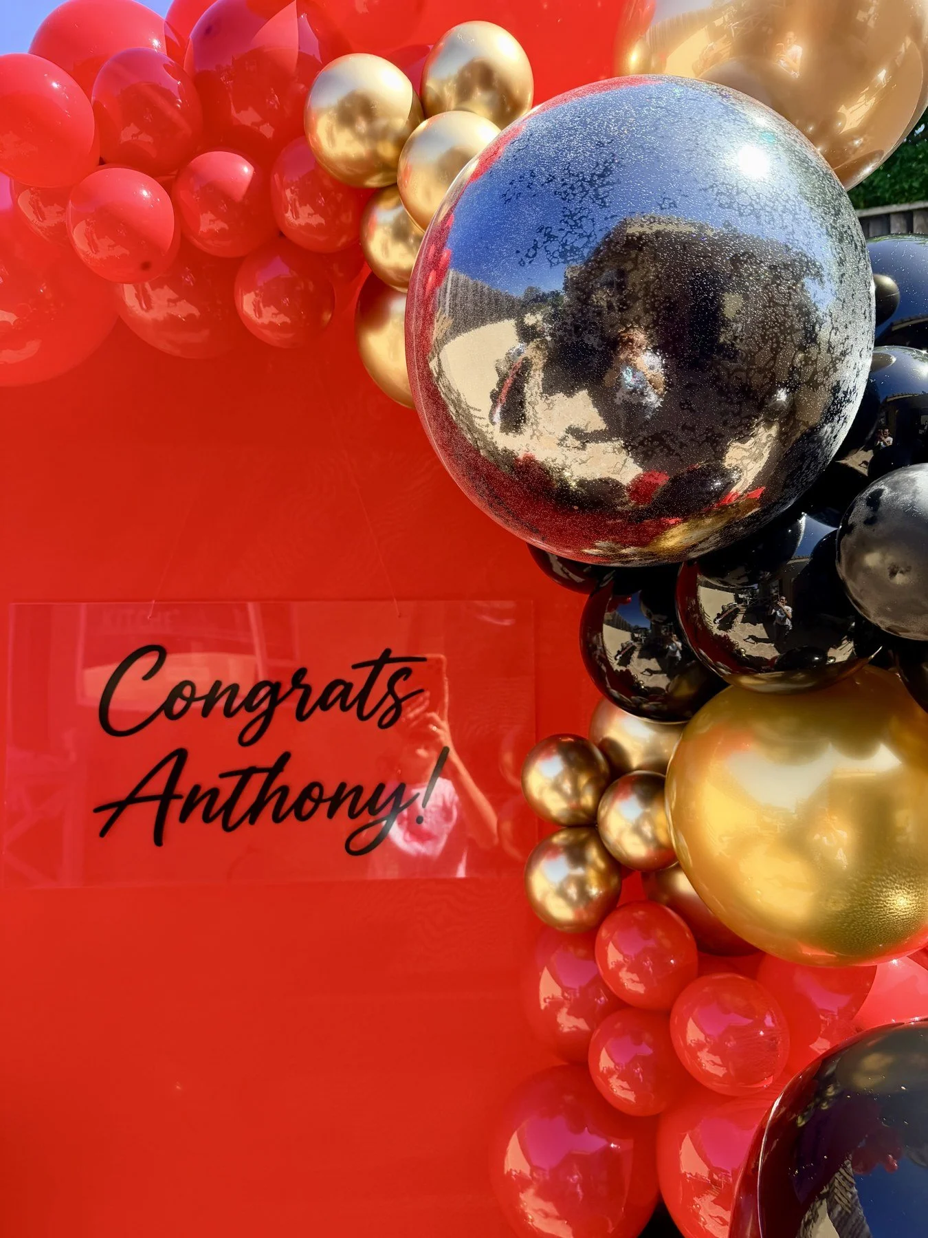 Custom Congrats Anthony lettering and reflective silver balloons on a red graduation backdrop in Hayward.