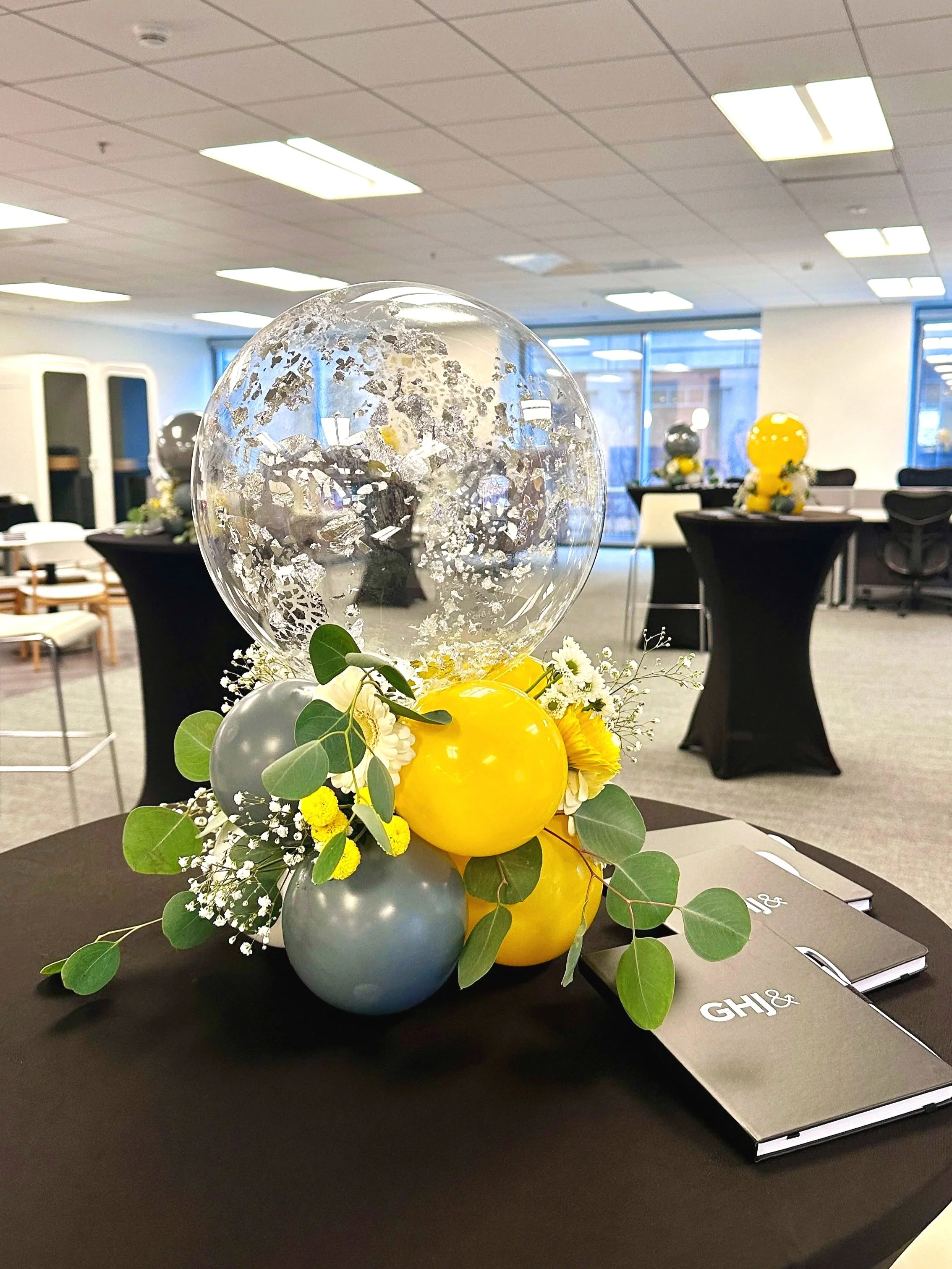 Modern corporate balloon and floral centerpiece with yellow balloon, eucalyptus and fresh flowers for office table decor in the Bay Area.