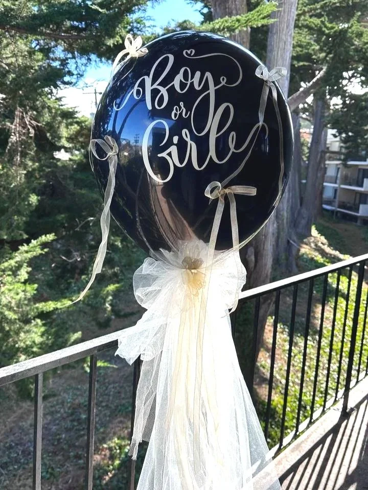 Large black balloon with "Boy or Girl" inscription, decorated with white tulle, used for a gender reveal celebration in the Bay Area