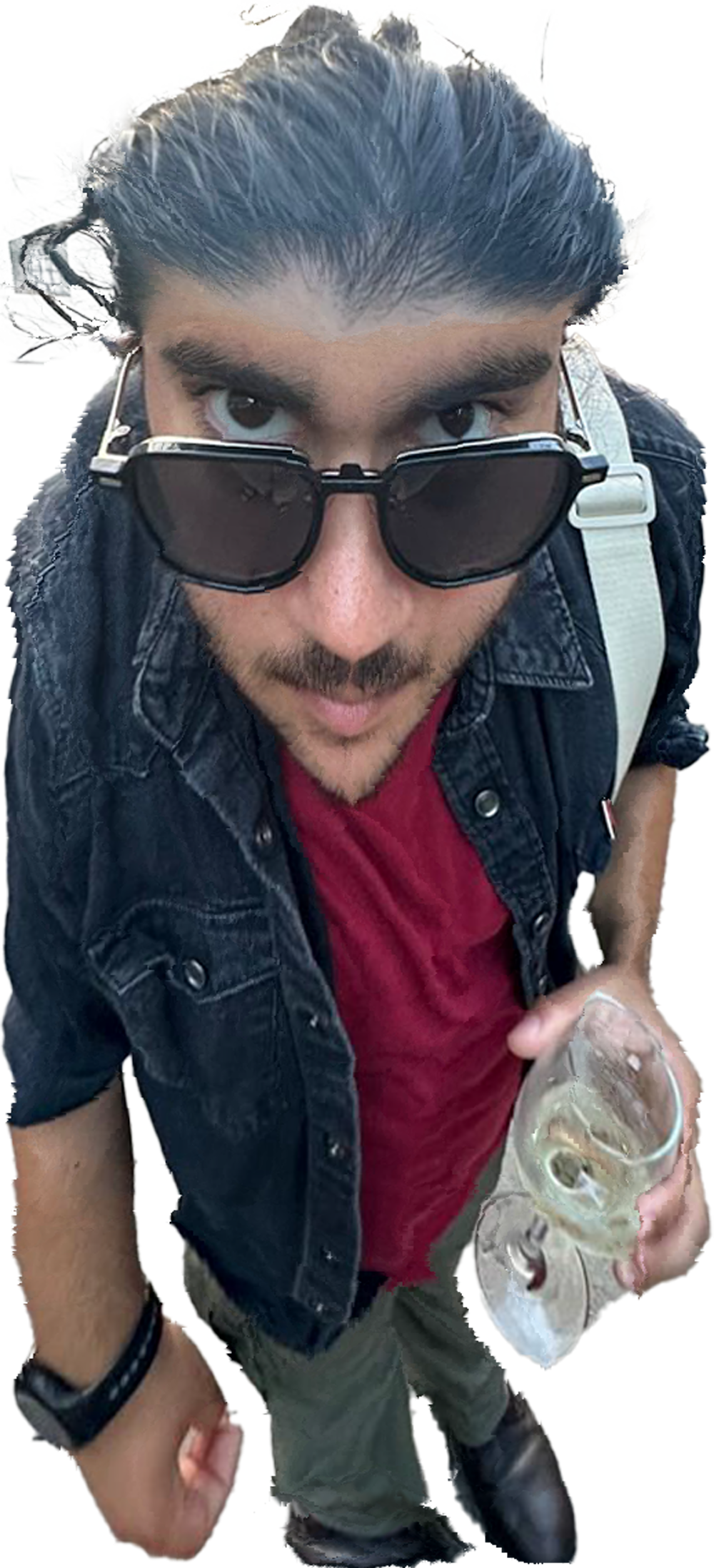 Hombre con gafas de sol oscuras y cabello oscuro peinado hacia atrás, usando una chaqueta de mezclilla negra y una camiseta roja, sosteniendo un vaso con bebida y hielo, visto desde arriba.