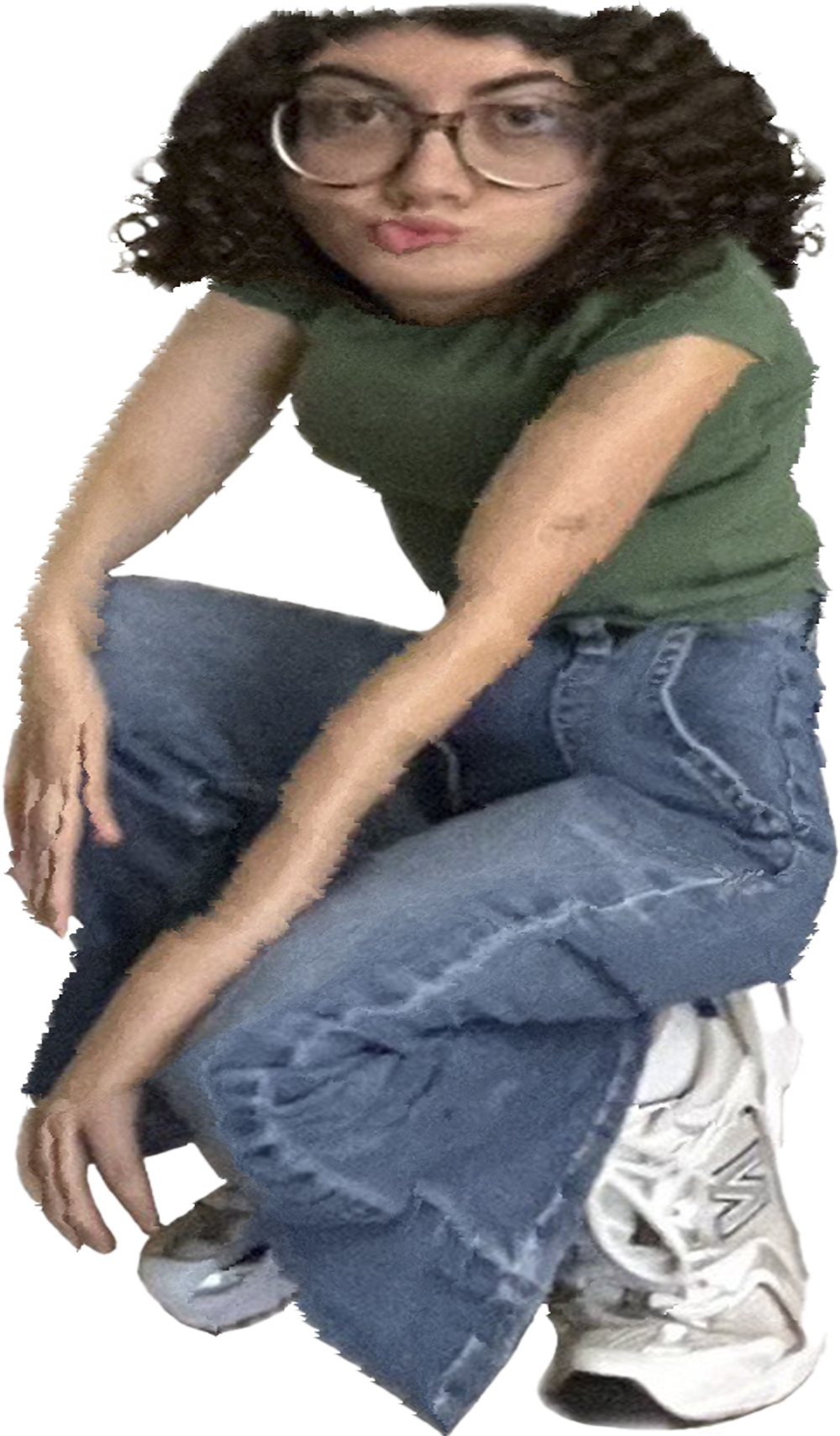 Una persona con el cabello rizado, gafas grandes, camiseta verde, jeans y zapatillas blancas, en posición de cuclillas.