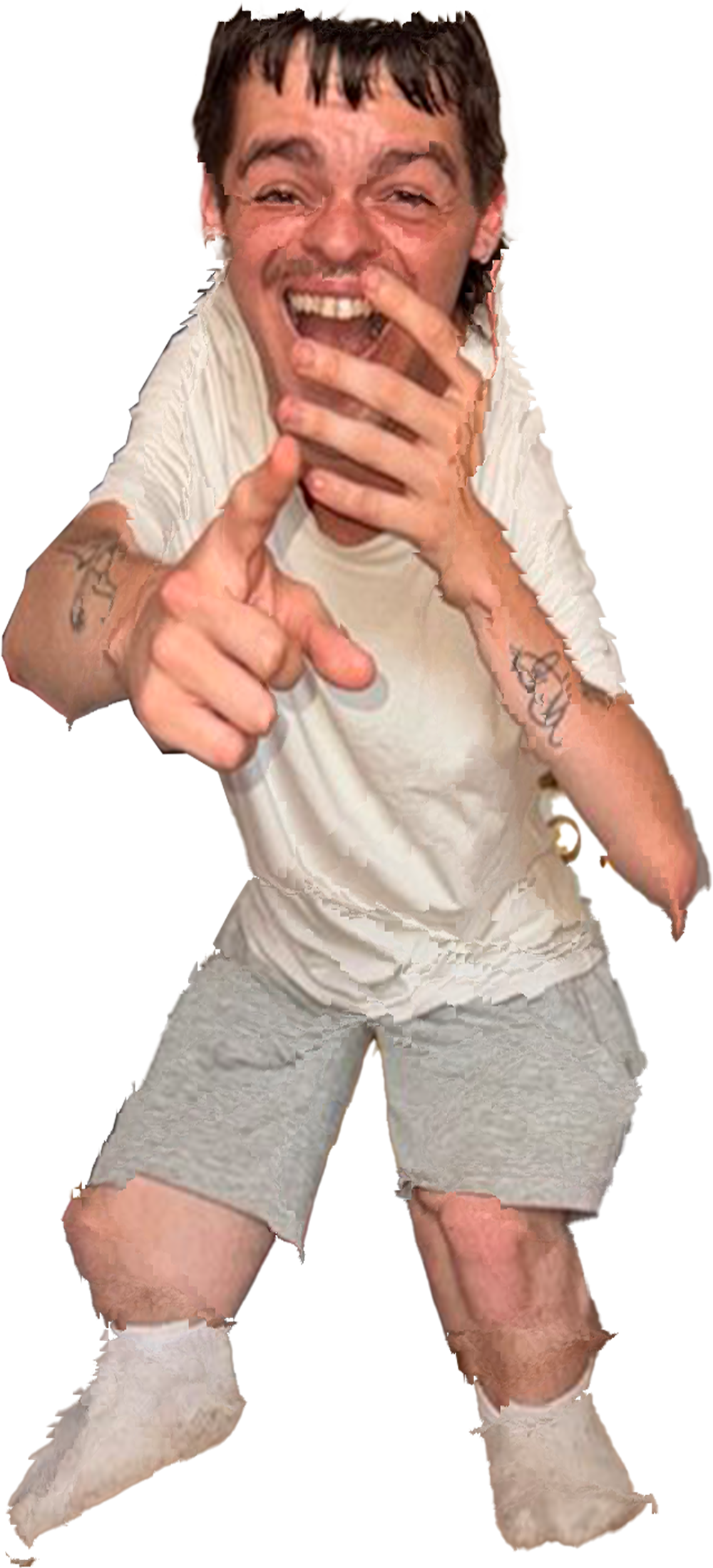 Hombre joven sonriendo, usando ropa blanca y calcetines, apuntando con un dedo, con tatuajes en los brazos, y expresión de alegría.