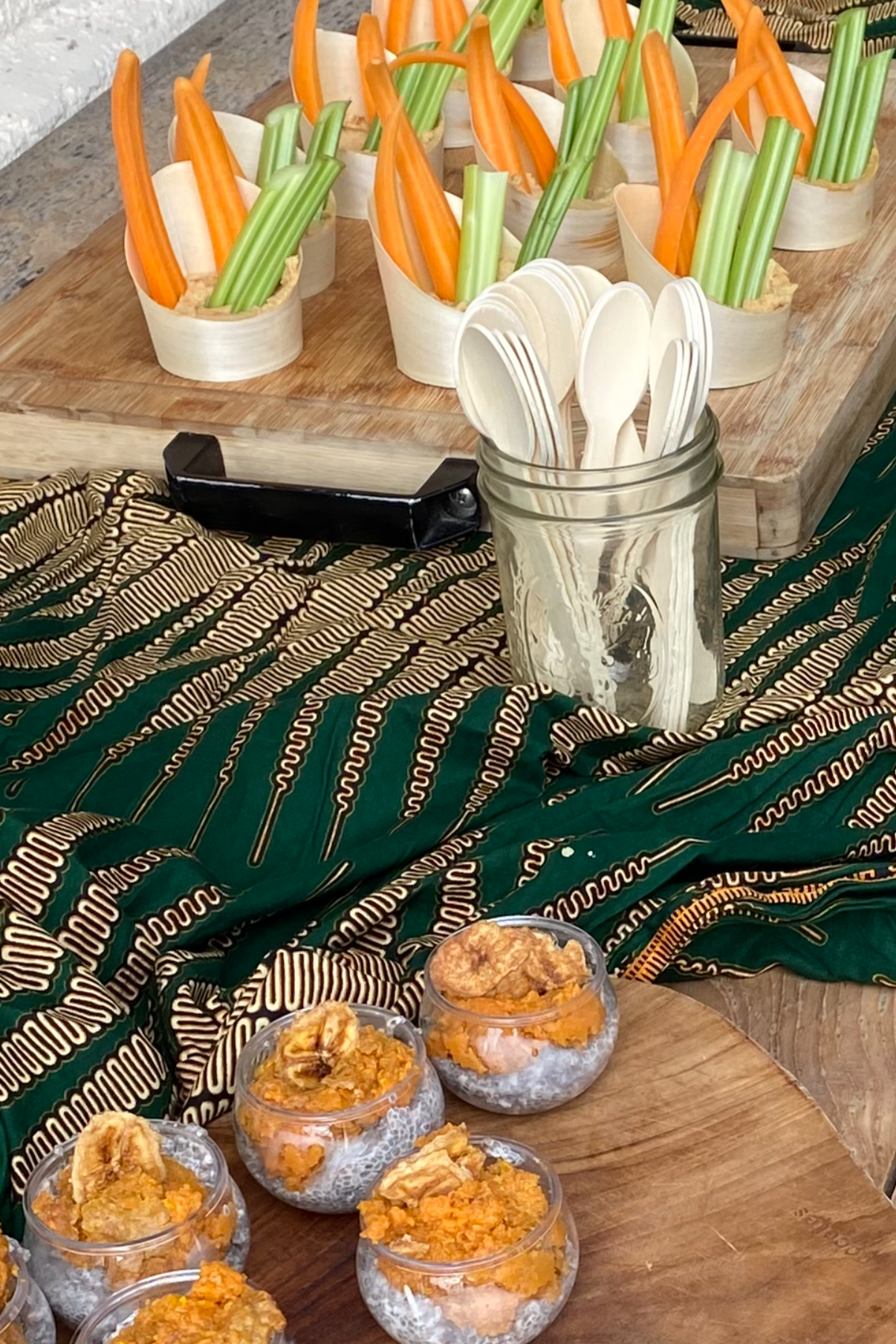 Individual servings of hummus topped with sliced carrots, celery sticks, and pita chips on a wooden table.